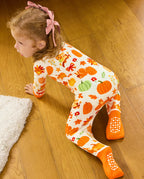 Rear view of a child crawling on a wooden floor, showing orange foot cuffs and white sole grips.