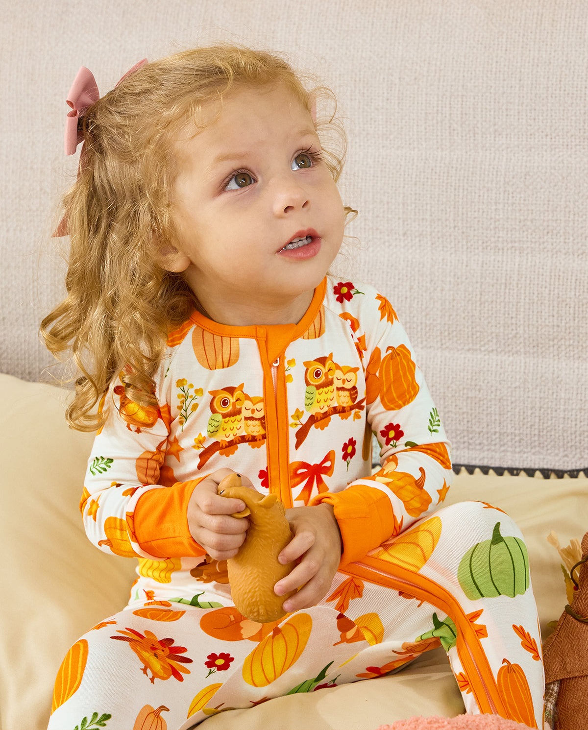 Close-up of a seated child holding a pinecone toy in the Pumpkin Patch romper.