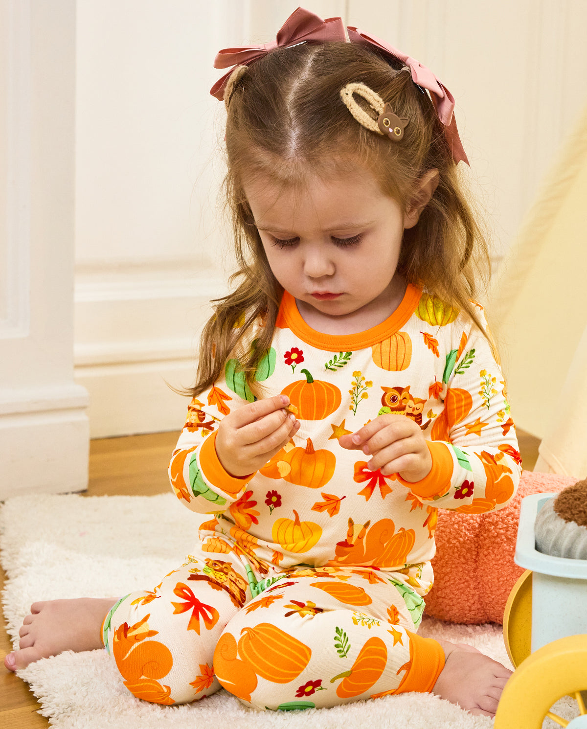 Child seated holding a pinecone in Pumpkin Patch pajamas with orange cuffs.