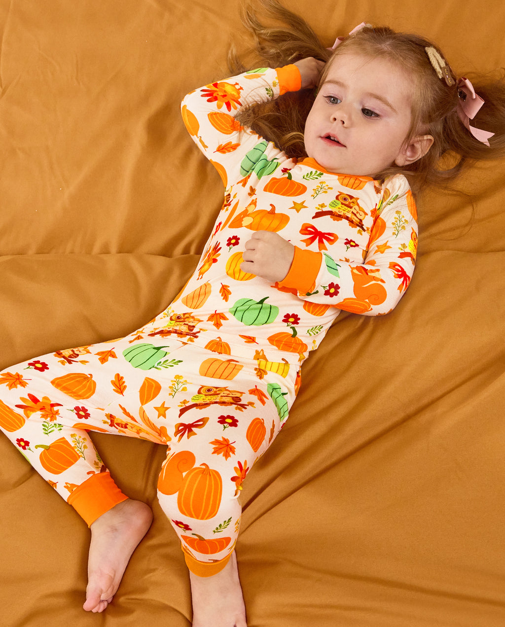 Child lying on orange bedding with an arm raised in Pumpkin Patch pajamas.