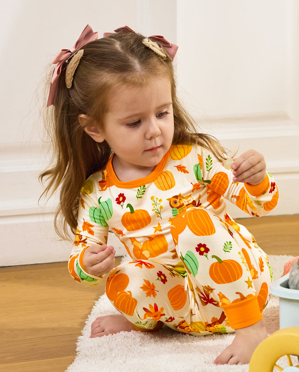 Child seated and looking down at a pinecone in Pumpkin Patch pajamas.