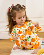 Child seated and looking down at a pinecone in Pumpkin Patch pajamas.
