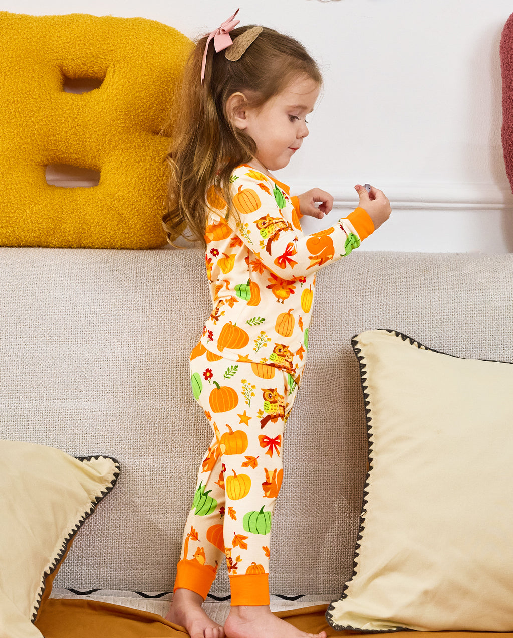 Side and rear view of a seated child holding a pinecone in Pumpkin Patch pajamas.