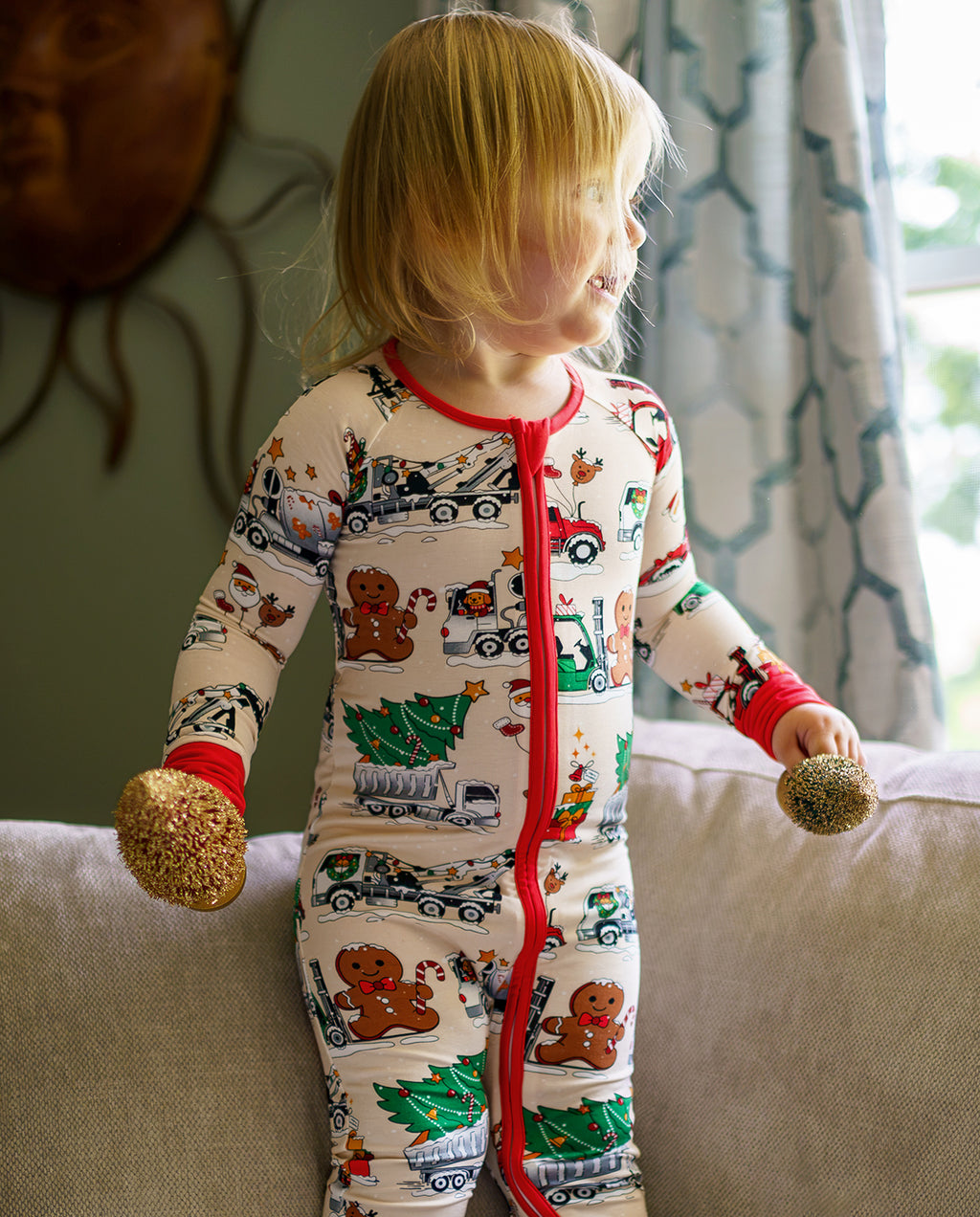Child standing on a sofa in Santa Express zippy while holding round ornaments