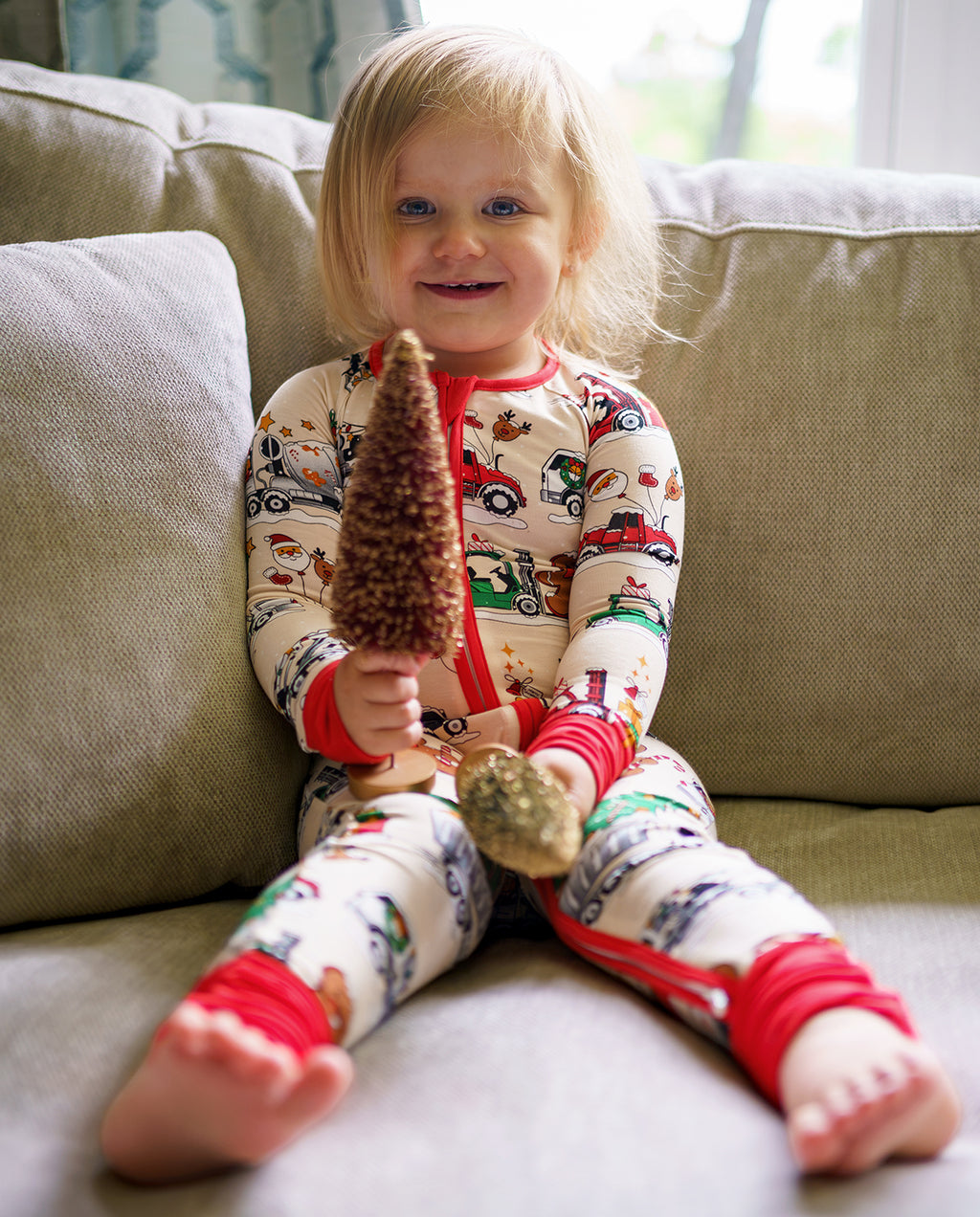 Smiling child sitting on a sofa in Santa Express zippy and holding a decorative tree