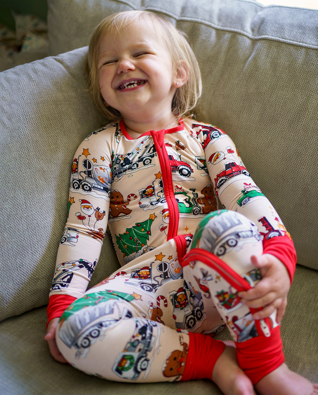 Laughing child sitting on a sofa in Santa Express cream and red zippy