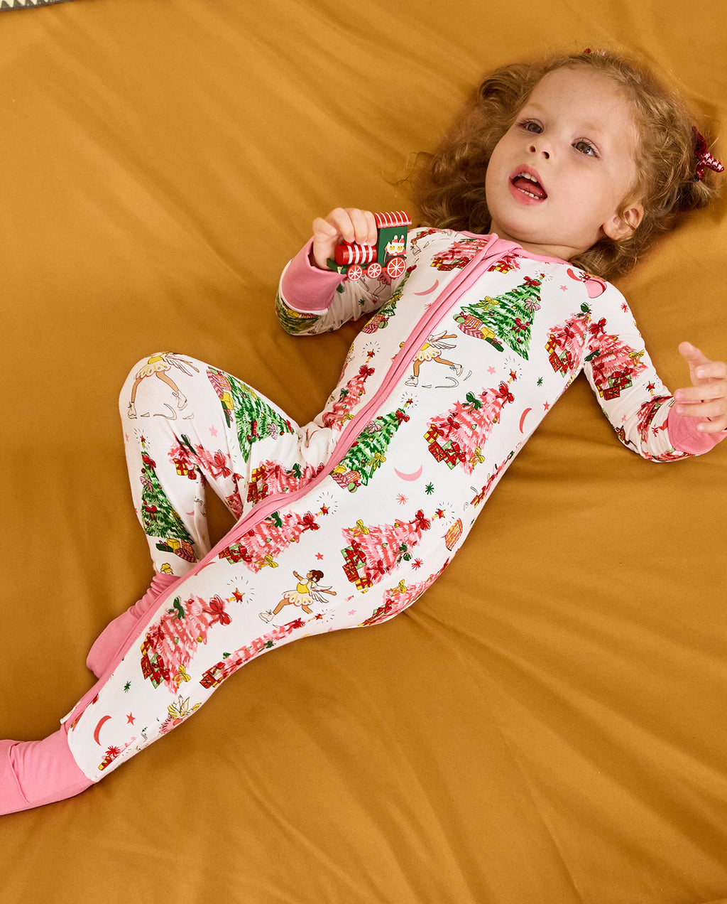 Child reclining on orange bedding with a toy train in the Snuggle Sparkle romper.