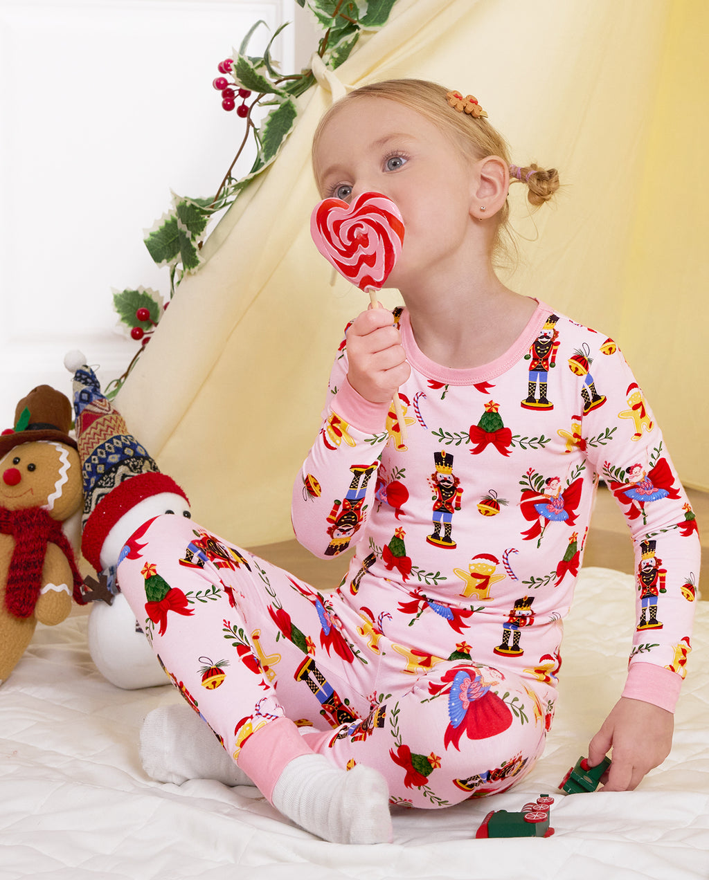 Child seated by a holiday play tent with a swirl lollipop in Sugarplum Wishes pajamas.