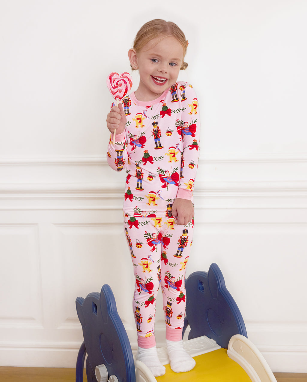 Smiling child standing on a slide with a lollipop in the Sugarplum Wishes pajama set.