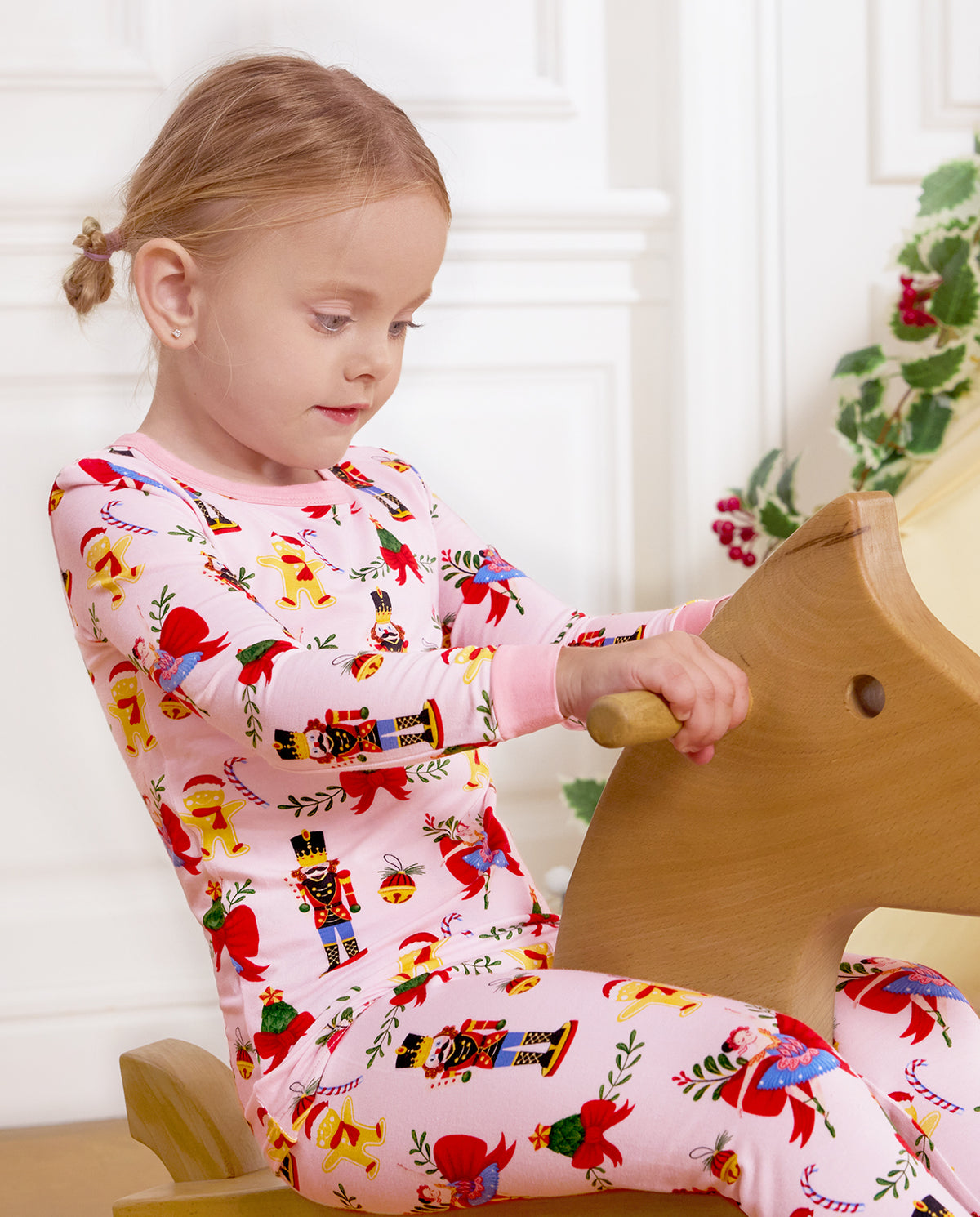 Side view of a child seated on a wooden rocking horse in Sugarplum Wishes pajamas.