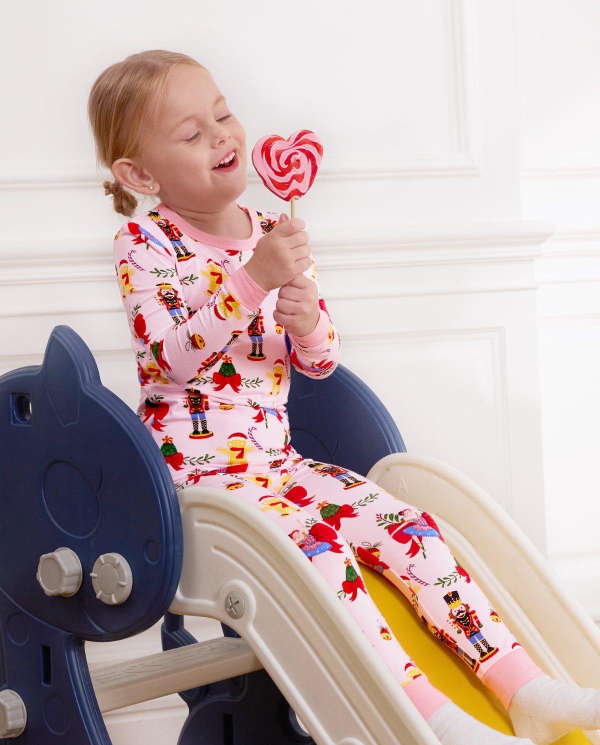 Child laughing with a lollipop while seated on a slide in Sugarplum Wishes pajamas.