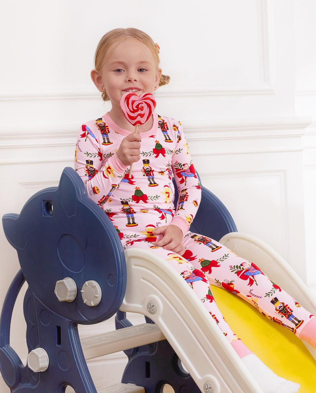 Child seated on a slide holding a lollipop in the Sugarplum Wishes two-piece set.