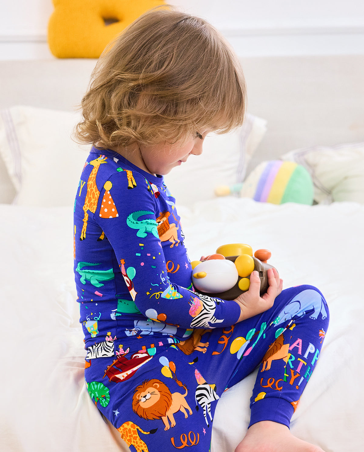 Side view of a child seated on a bed in Birthday Safari pajamas