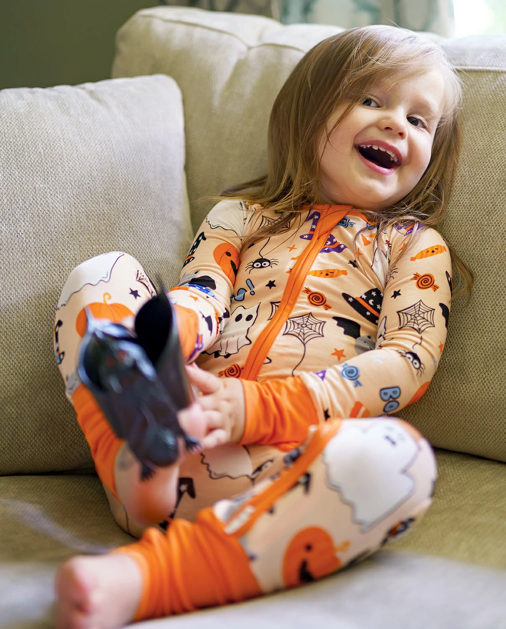 Child smiling on a couch in Boo Treats Bamboo Zippy with Halloween ghost and pumpkin print