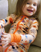 Child smiling in Boo Treats Bamboo Zippy on a couch with Halloween pumpkin and ghost print