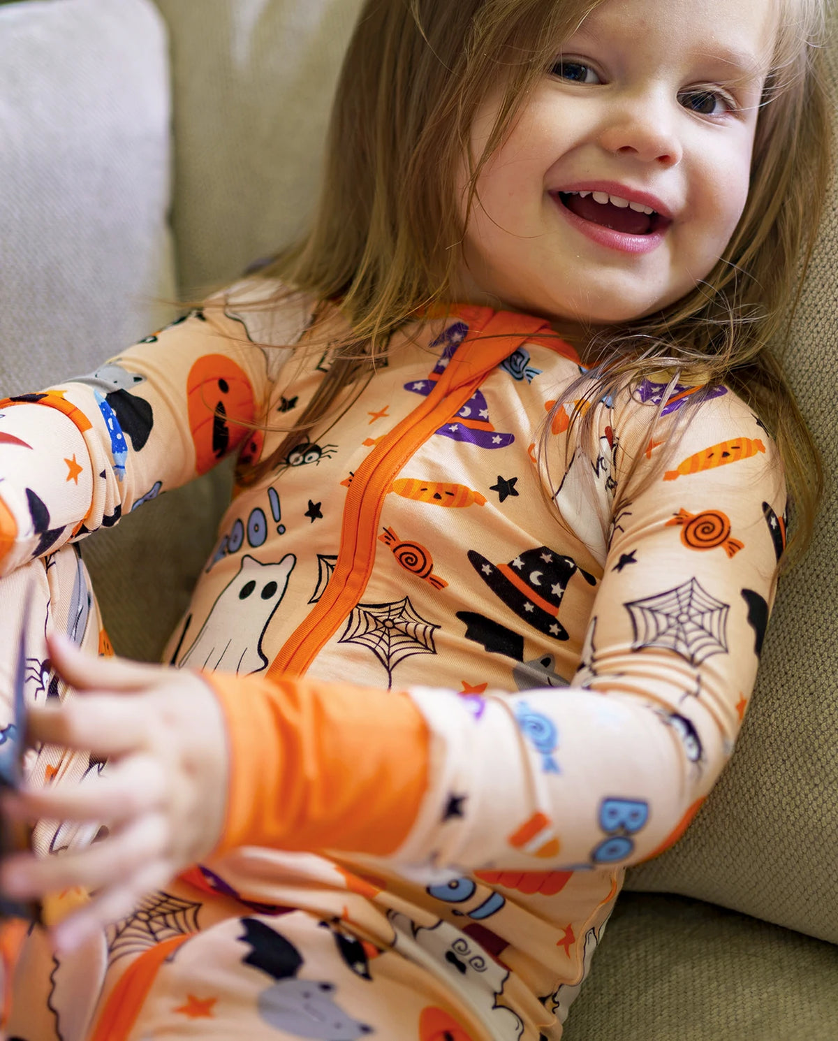 Child smiling in Boo Treats Bamboo Zippy on a couch with Halloween pumpkin and ghost print