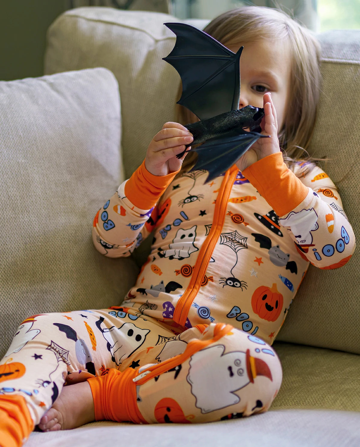 Child holding black bat toy while wearing Boo Treats Bamboo Zippy Halloween pajamas