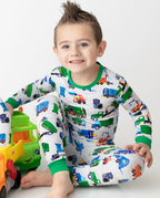 Child seated beside toy trucks in Garbage Squad pajamas