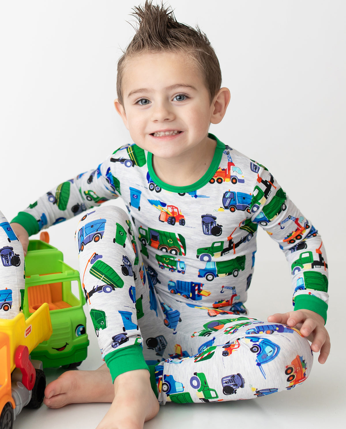 Child seated beside toy trucks in Garbage Squad pajamas