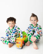 Two children seated with toy trucks in grey truck-print pajamas