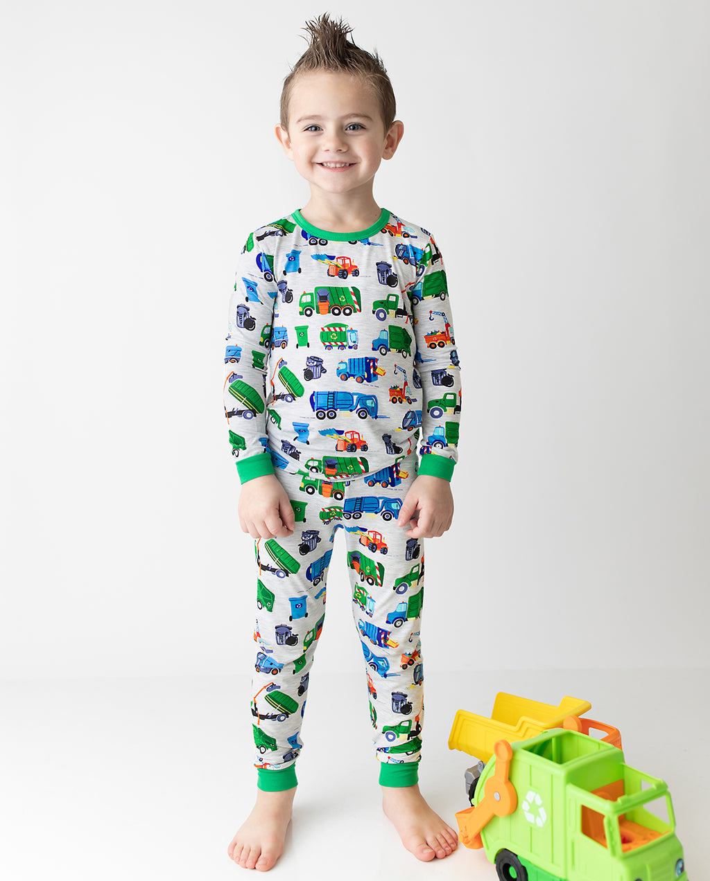 Child standing beside toy trucks in grey Garbage Squad pajamas