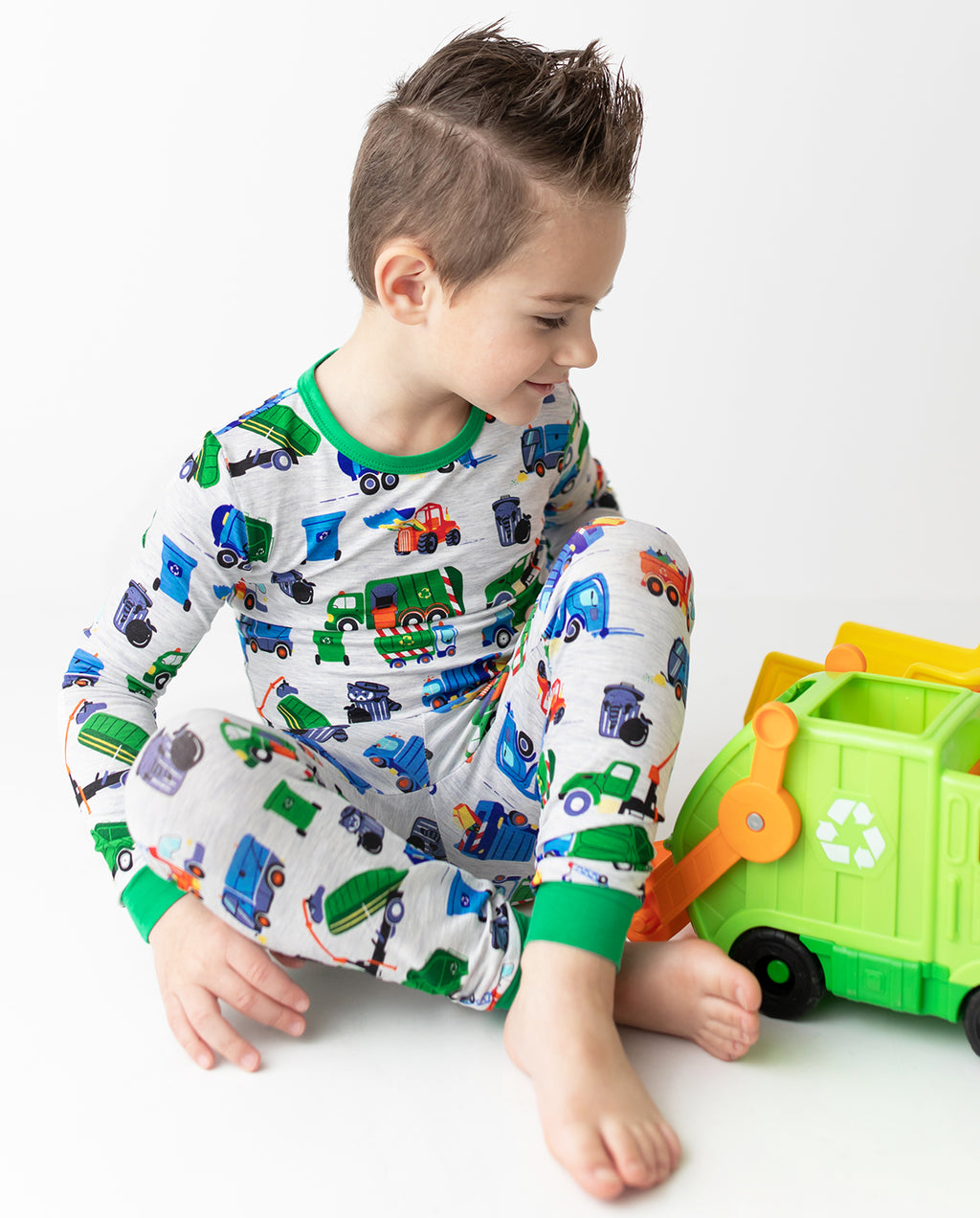 Child playing with a green toy truck in Garbage Squad pajamas