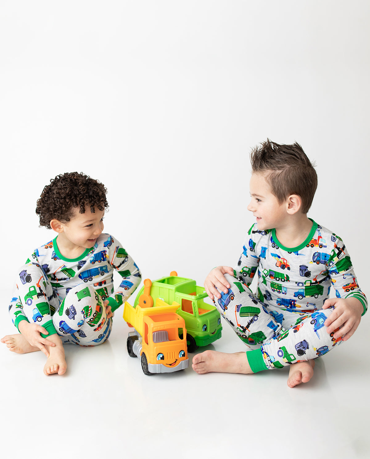 Two children playing with toy trucks in Garbage Squad pajamas