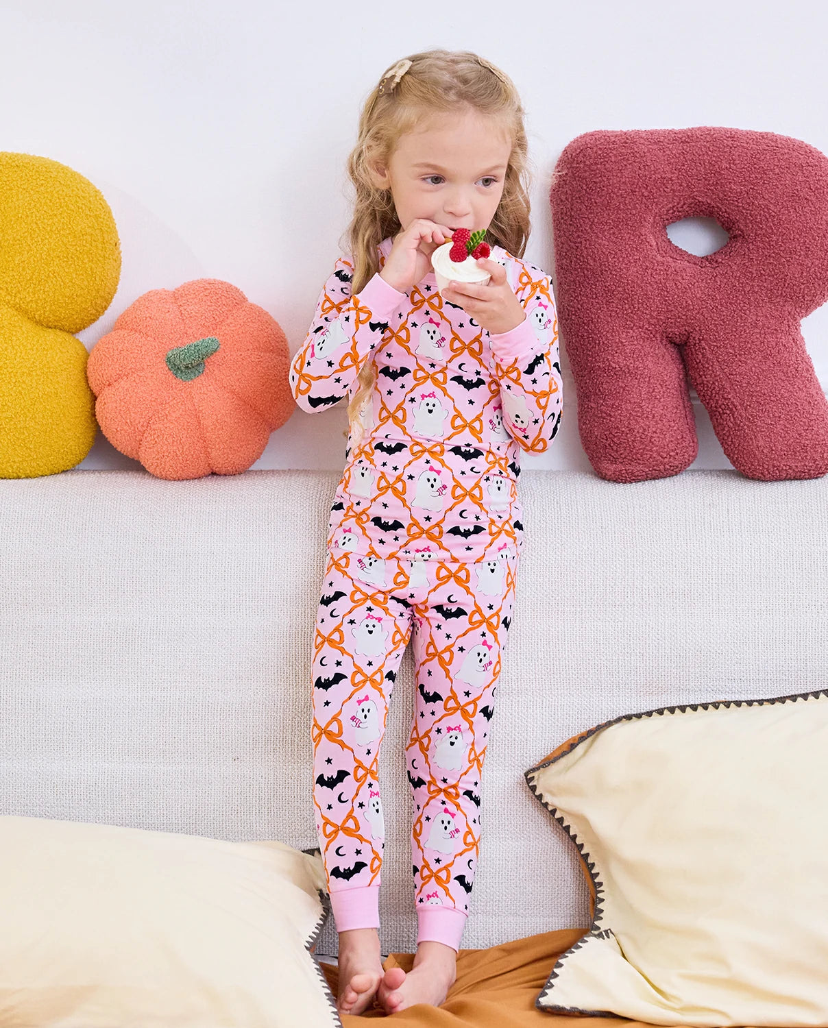 Ghost Bows Long Two-Piece Pajama Set - child wearing the ghost-and-bow pajamas while eating a lollipop