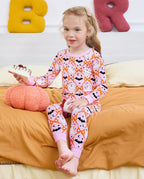 Ghost Bows Long Two-Piece Pajama Set - child wearing the ghost-and-bow pajamas while seated on a bed