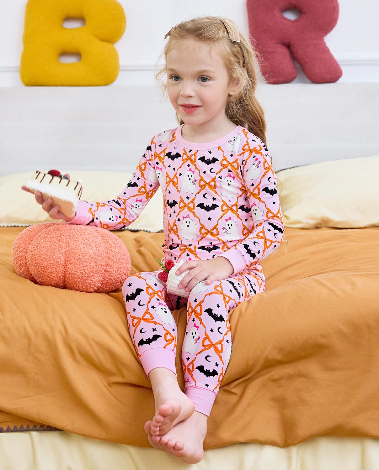 Ghost Bows Long Two-Piece Pajama Set - child wearing the ghost-and-bow pajamas while seated on a bed