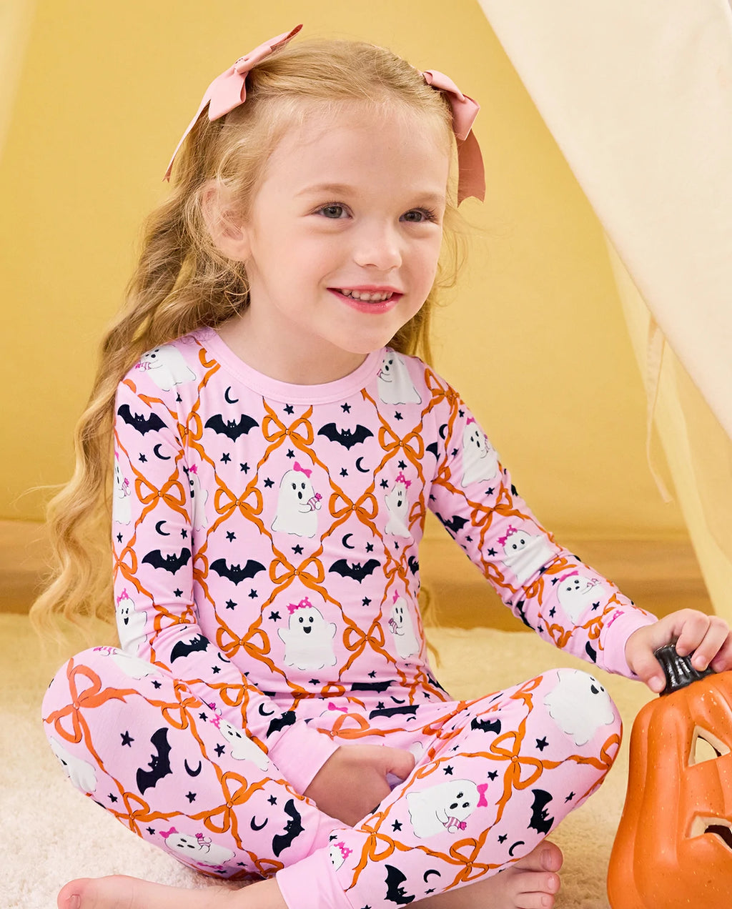 Ghost Bows Long Two-Piece Pajama Set - child wearing the ghost-and-bow pajamas while seated with a pumpkin bucket