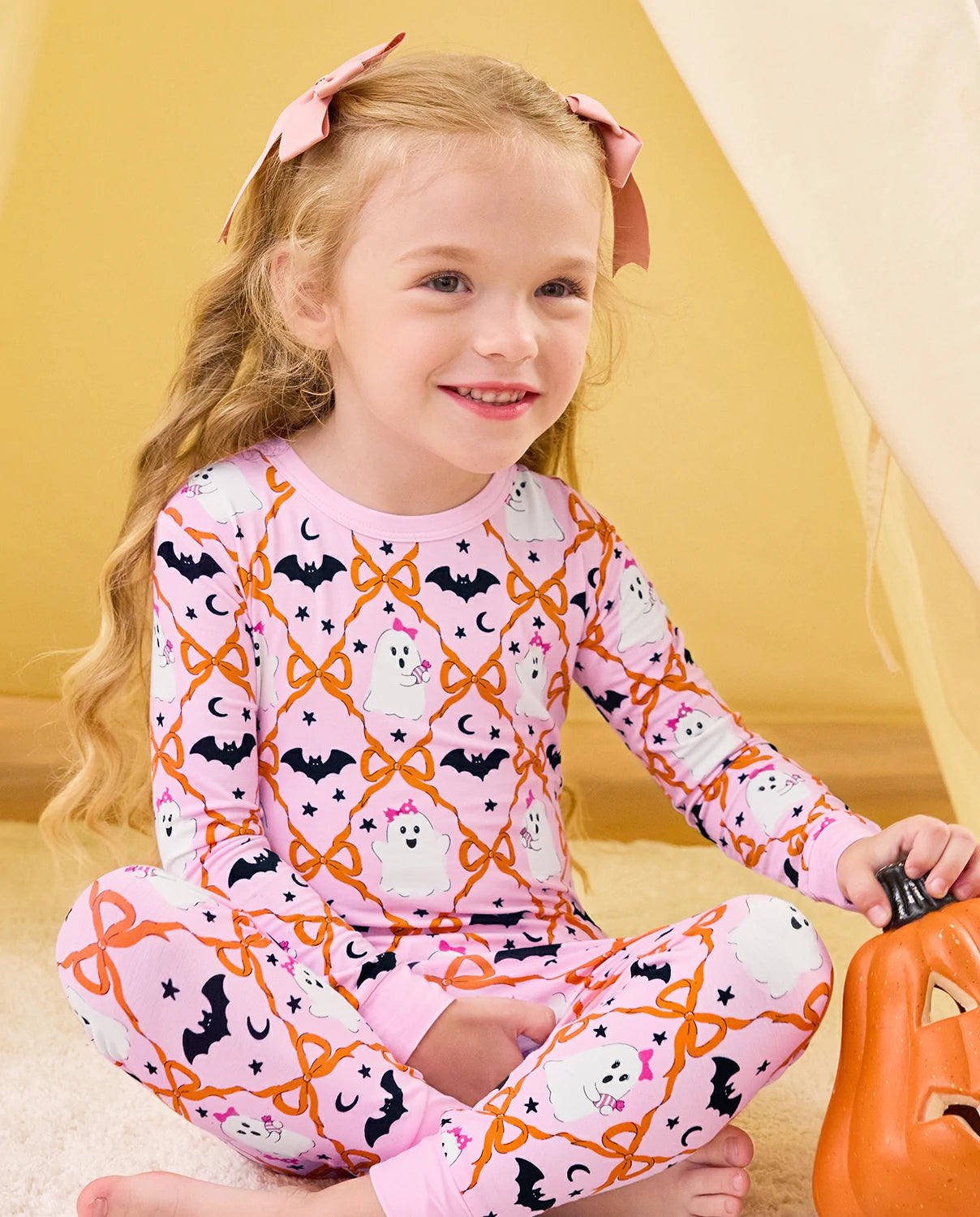 Ghost Bows Long Two-Piece Pajama Set - child wearing the ghost-and-bow pajamas while seated with a pumpkin bucket