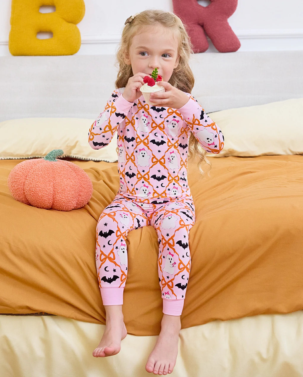 Ghost Bows Long Two-Piece Pajama Set - child wearing the ghost-and-bow pajamas while seated with a lollipop