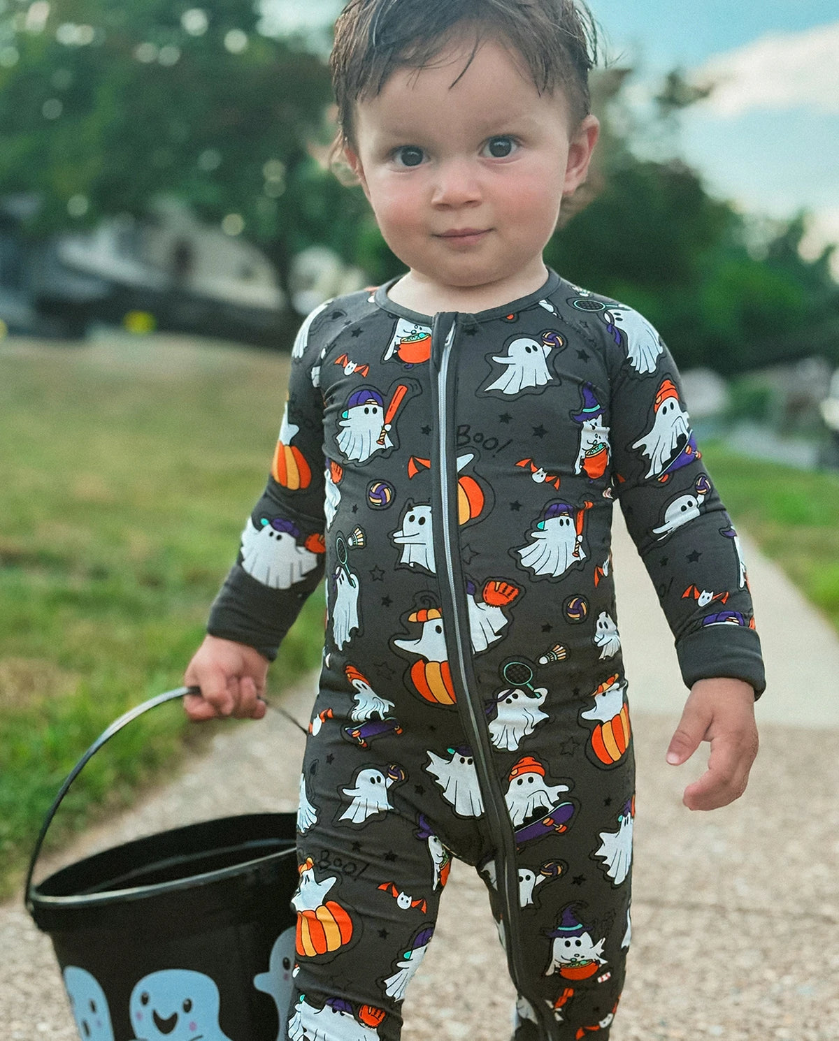 Toddler wearing Ghostie Sports Club Bamboo Zippy standing outdoors in a dark Halloween ghost print zippy