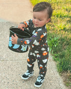 Toddler wearing Ghostie Sports Club Bamboo Zippy standing outdoors with a Halloween bucket