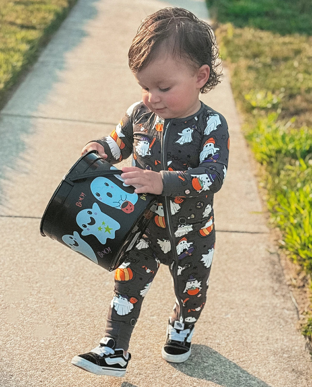 Toddler wearing Ghostie Sports Club Bamboo Zippy walking outdoors with a Halloween ghost trick-or-treat bucket