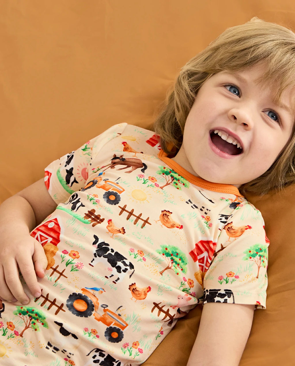 Happy Farmyard Short Two-Piece Pajama Set - child wearing the short pajamas while reclining and laughing
