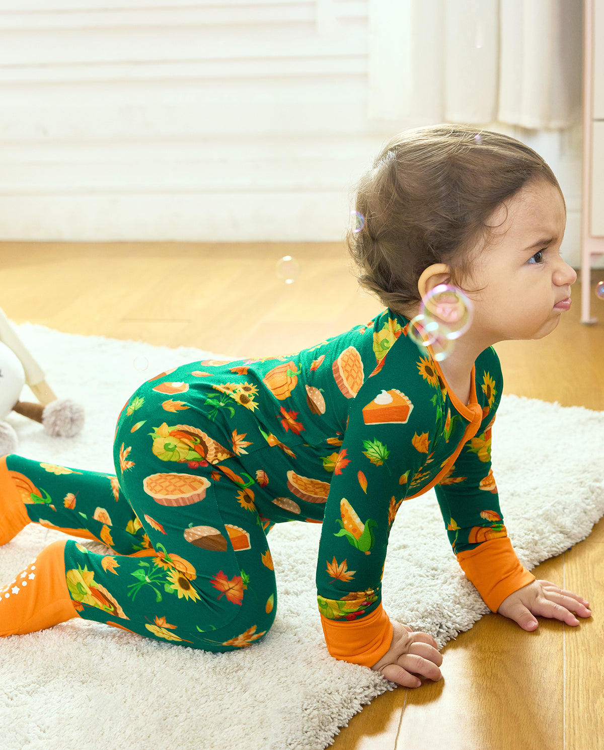 Side view of a baby crawling in Harvest Feast Bamboo Zippy with orange fold-over foot cuffs.
