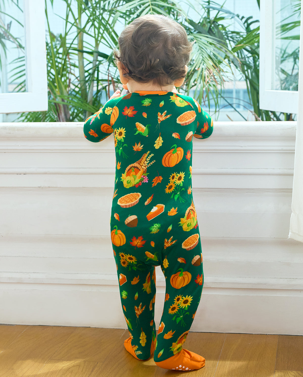 Full back view of a baby in Harvest Feast Bamboo Zippy by a window.