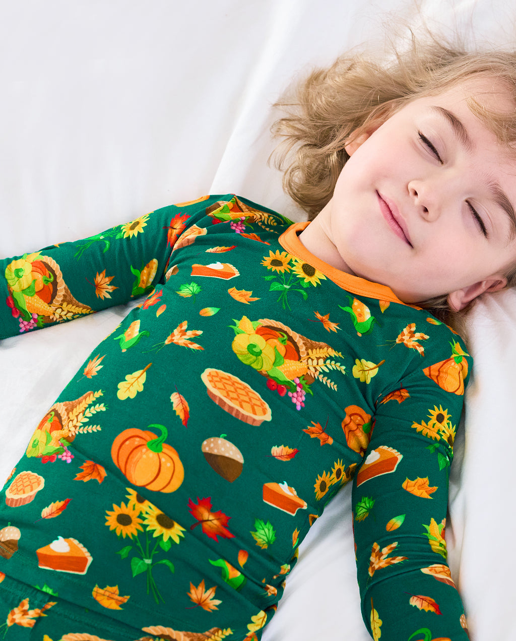Child resting in Harvest Feast long two-piece pajamas with orange trim.
