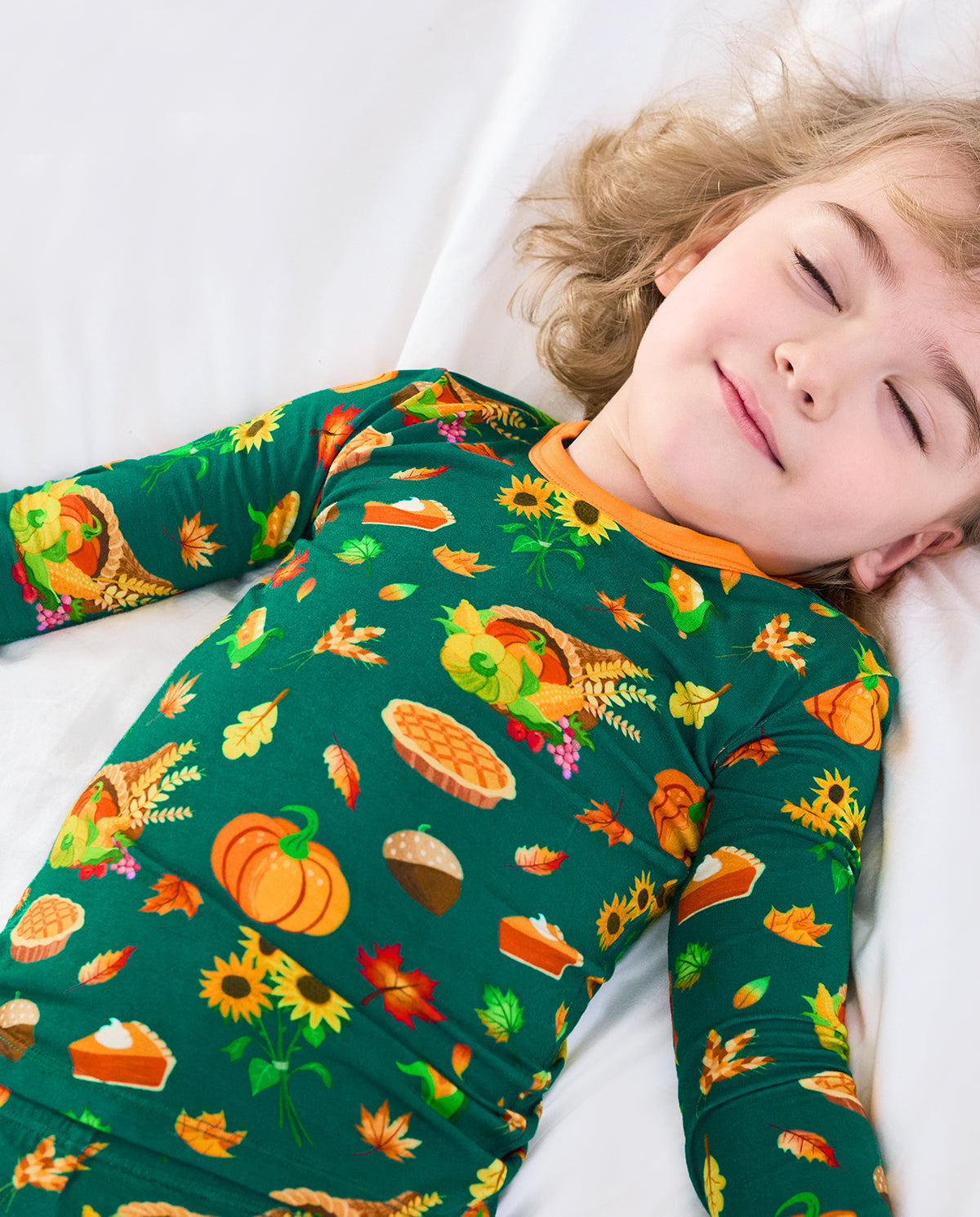 Child resting in Harvest Feast long two-piece pajamas with orange trim.