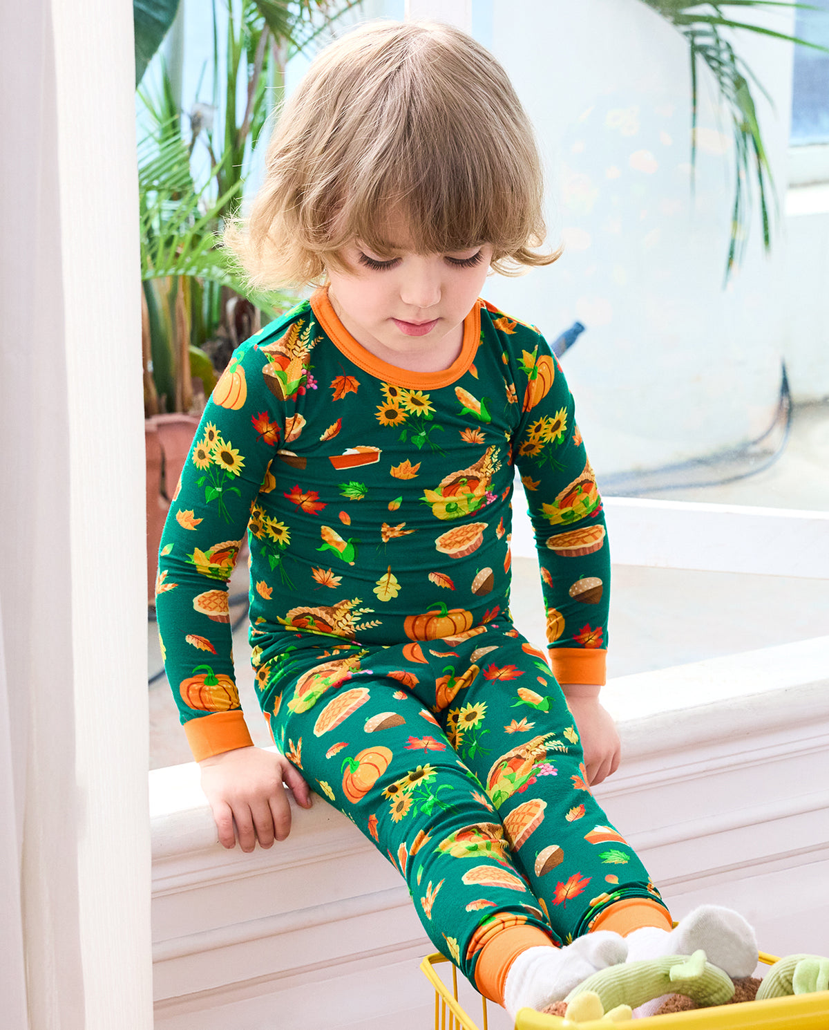 Child seated by a window in Harvest Feast long two-piece pajamas with orange trim.
