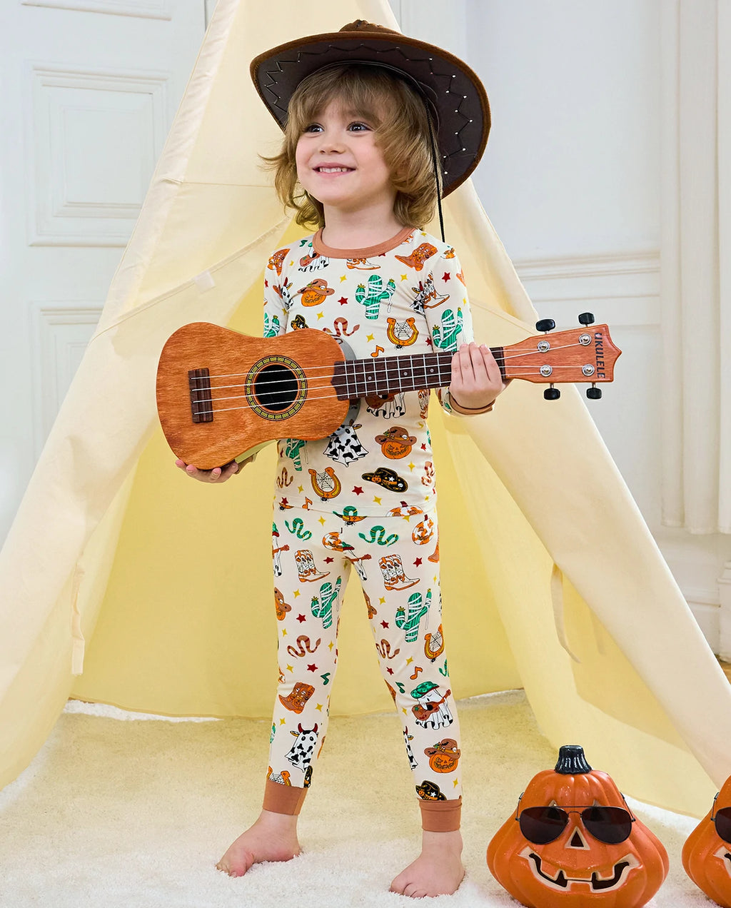 Howdy Halloween Long Two-Piece Pajama Set - child wearing the pajamas with a cowboy hat and ukulele, front view