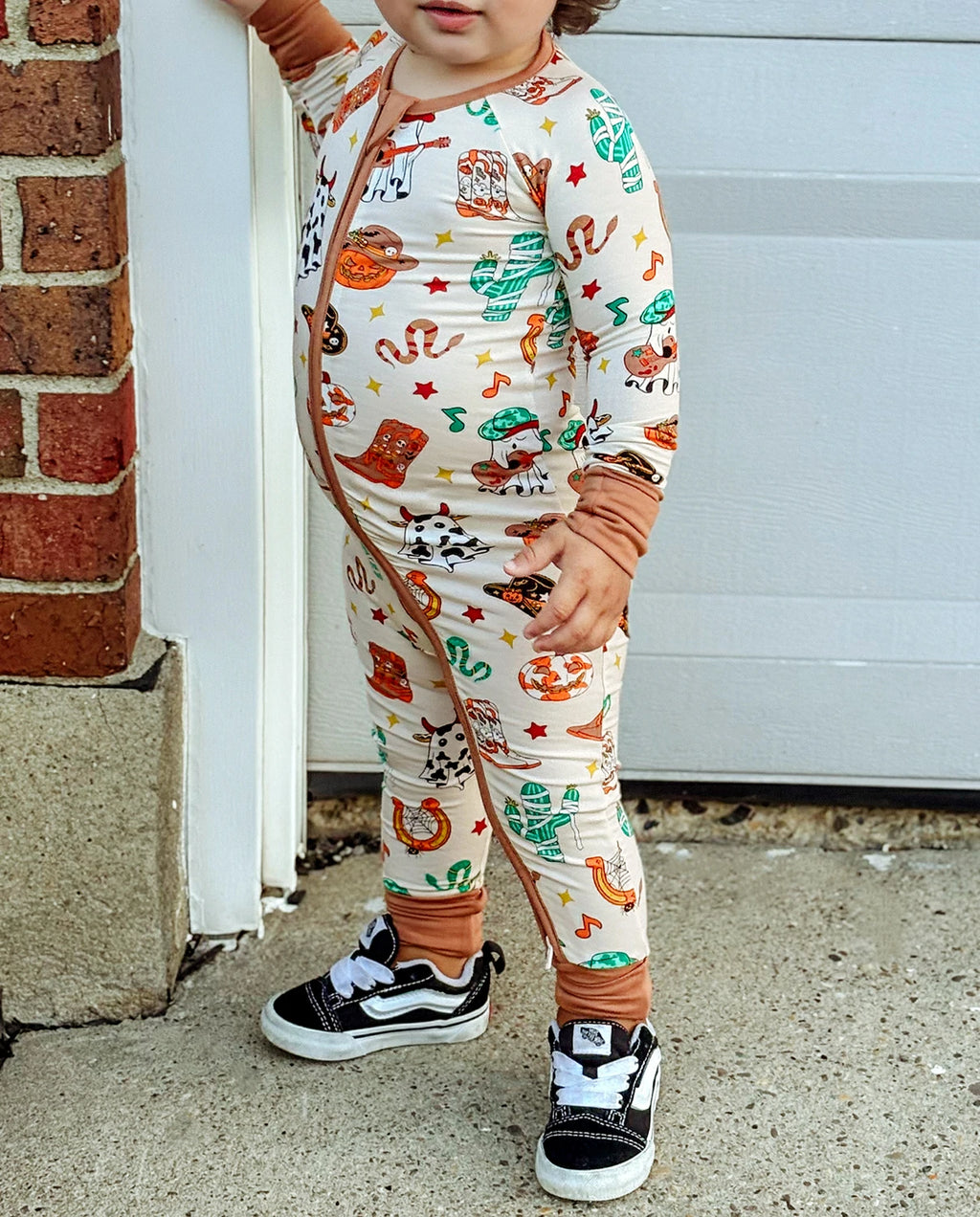 Child standing near a doorway in Howdy Halloween Bamboo Zippy with cowboy boots pumpkins and cactus print