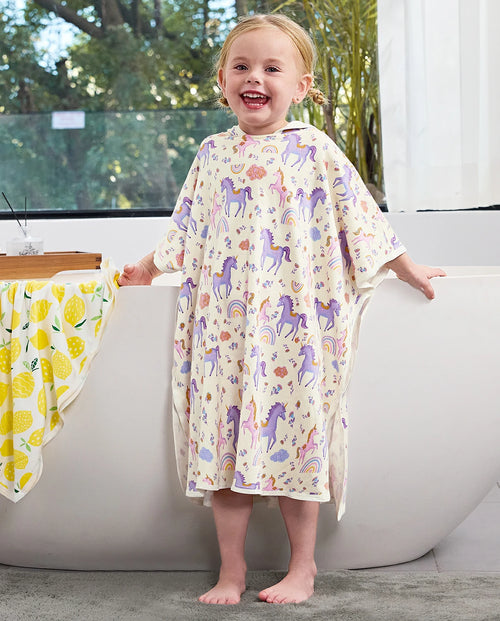 Lavender Unicorn Hooded Toddler Bath Towel - child wearing the unicorn-print hooded towel beside a bathtub, front view