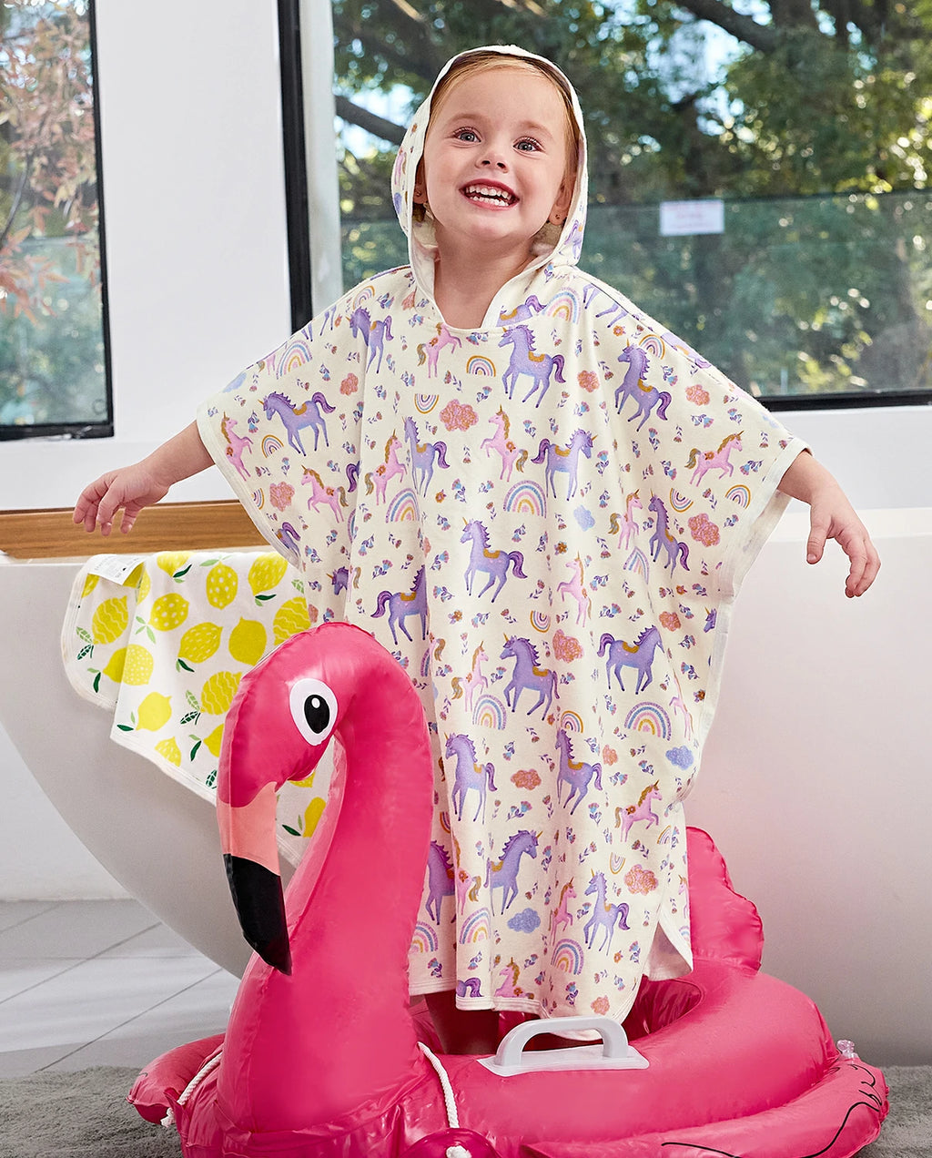 Lavender Unicorn Hooded Toddler Bath Towel - child wearing the hooded towel while seated on a flamingo pool float