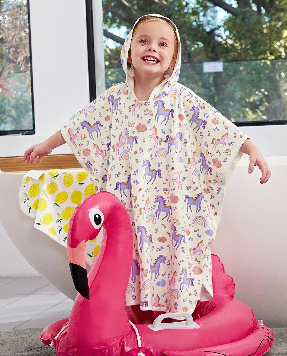 Lavender Unicorn Hooded Toddler Bath Towel - child wearing the hooded towel while seated on a flamingo pool float