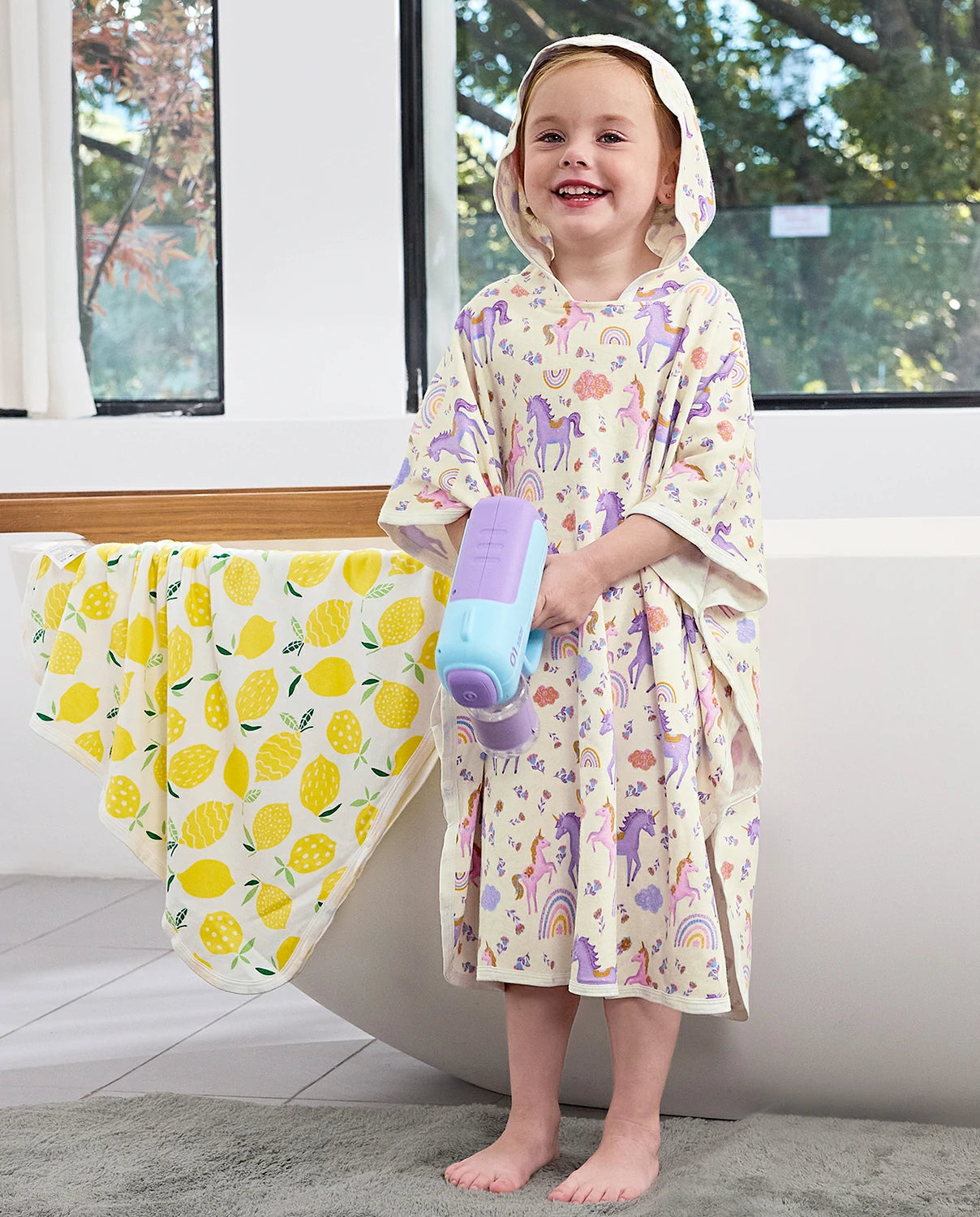 Lavender Unicorn Hooded Toddler Bath Towel - child wearing the hooded towel and holding a water toy, front view