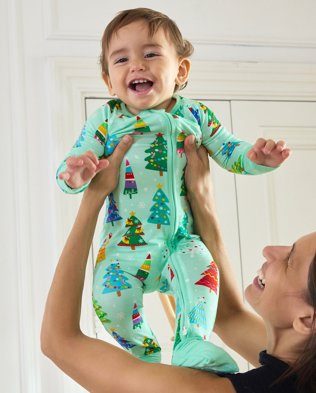 Baby held up wearing the mint-green Merry Trees Bamboo Zippy with colorful Christmas trees