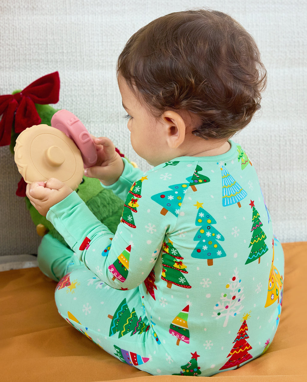 Seated baby showing the Christmas tree print on the back of the Merry Trees Bamboo Zippy